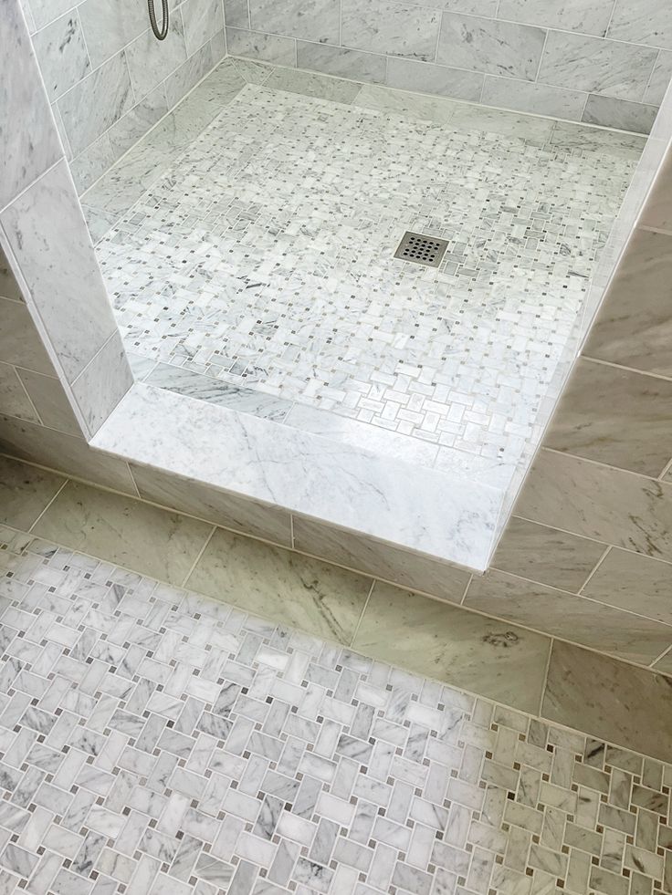 a walk in shower sitting next to a white tiled wall and floor with a glass door