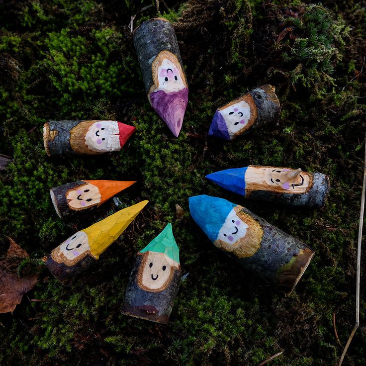 several wooden logs with painted faces are arranged in a circle on the mossy ground