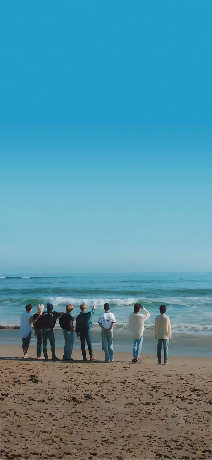 a group of people standing on top of a sandy beach next to the ocean under a blue sky