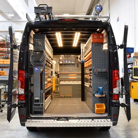 the back end of a van parked in a warehouse filled with shelves and other items