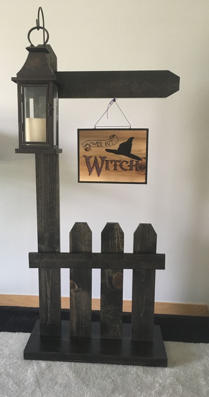 a wooden sign hanging from the side of a wall next to a fence with a candle