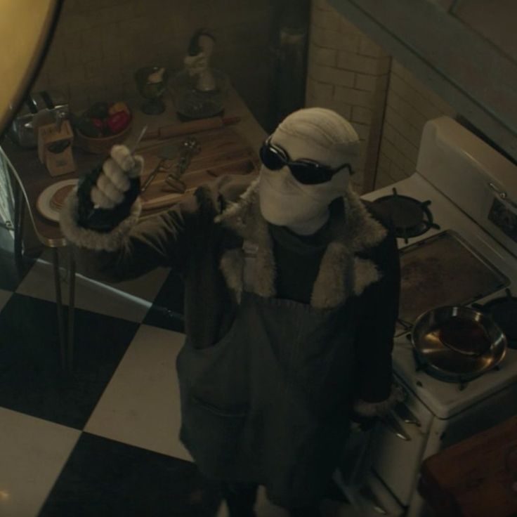 a person in a kitchen wearing a mask and holding something up to the camera with both hands