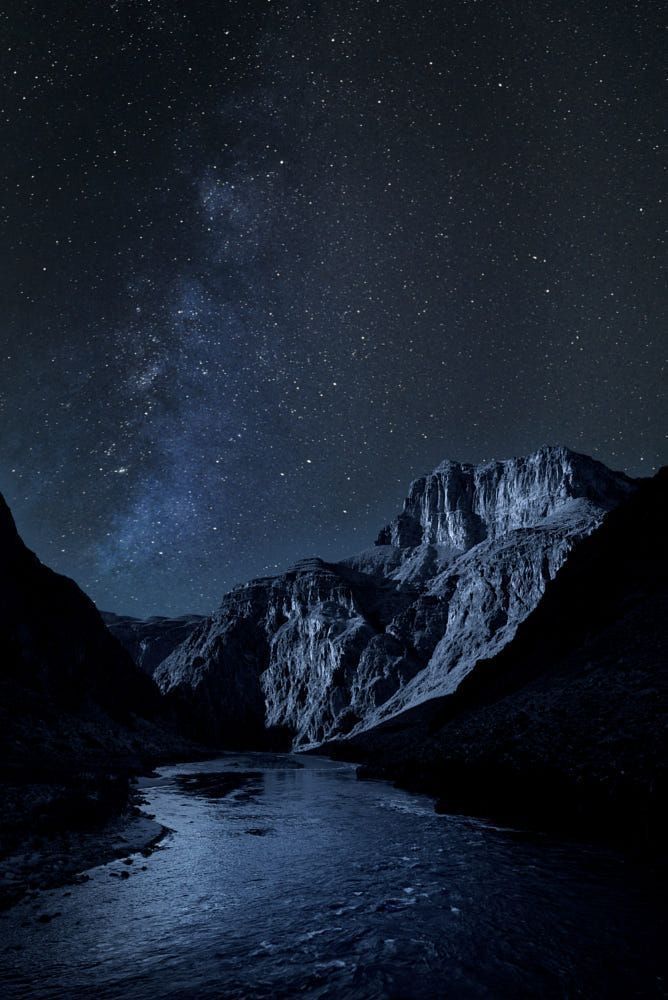 the night sky is filled with stars above mountains and a river in the foreground