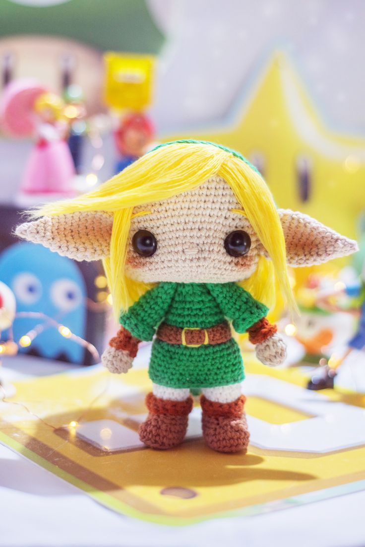 a crocheted elf doll standing on a table with other toys in the background