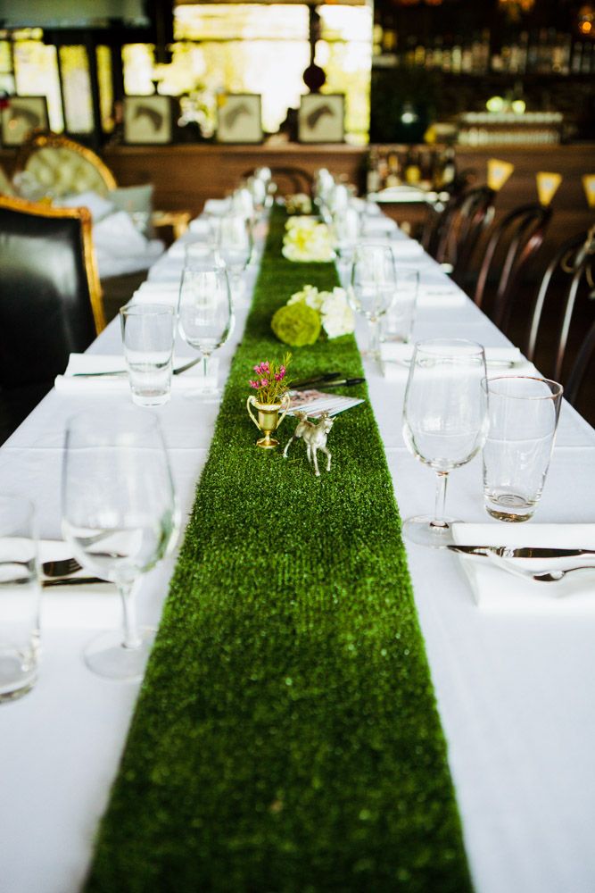 the long table is set with white linens and green grass runnering, along with empty wine glasses