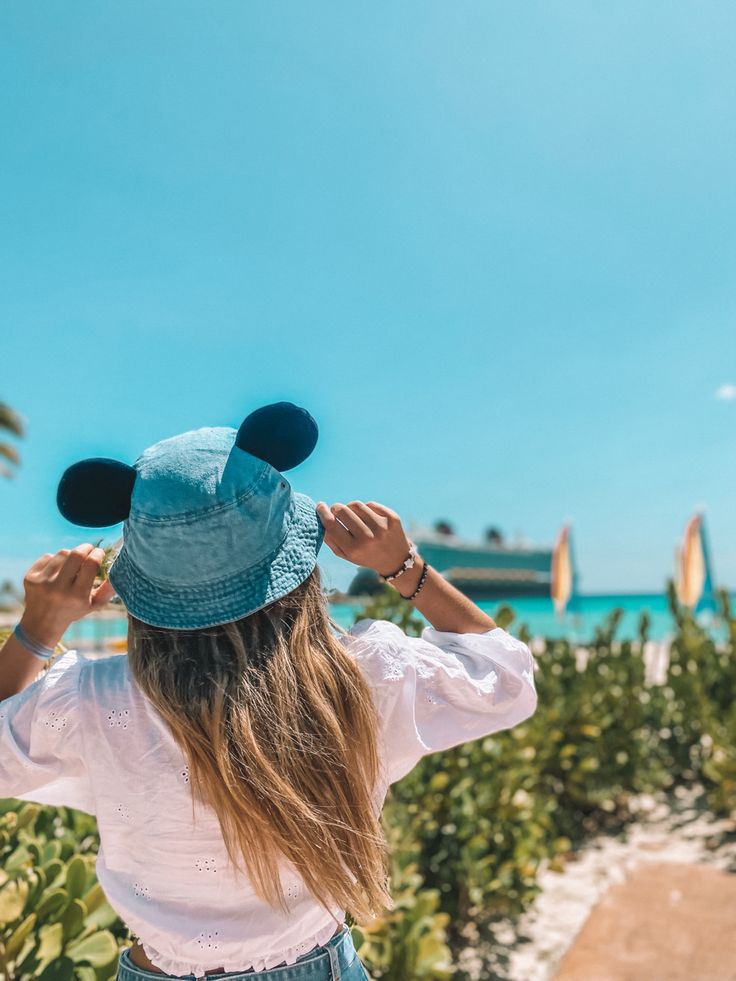 a woman with long hair wearing a blue mickey ears hat looking out at the ocean