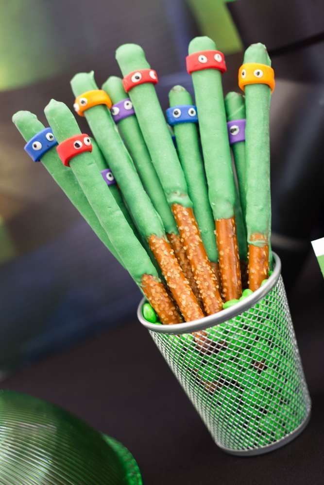 a cup filled with green and orange candy sticks covered in googly eyes, sitting on top of a table