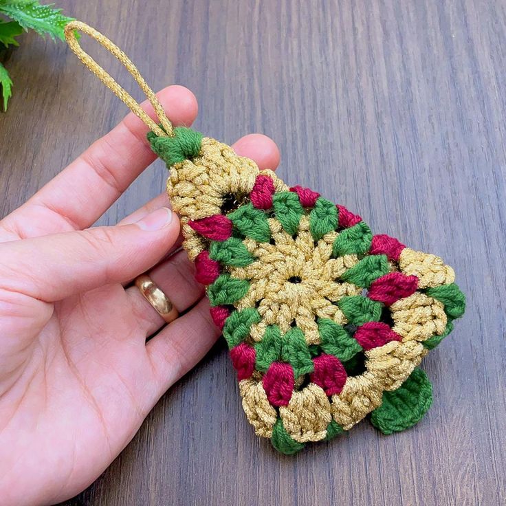 a hand is holding a crocheted ornament on a table next to a plant