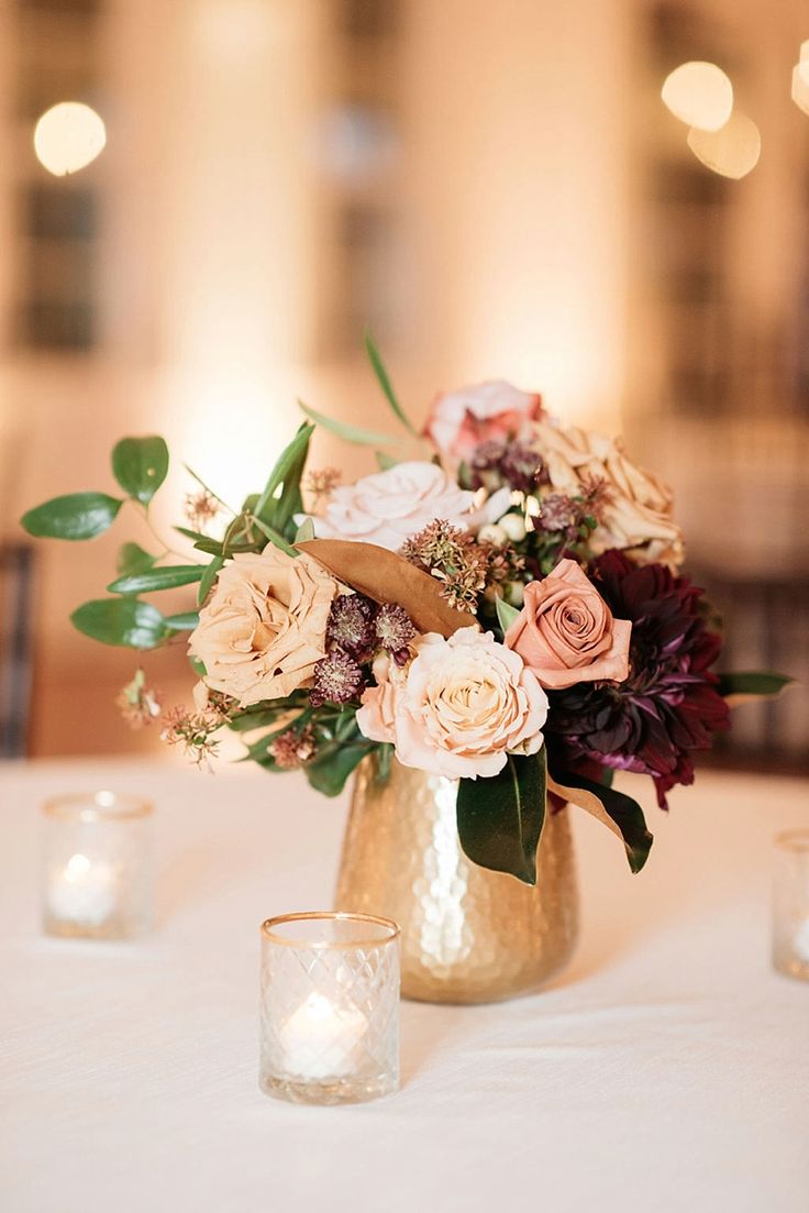 a vase filled with lots of flowers on top of a white table cloth next to candles