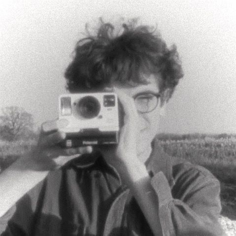 a man holding up a camera to take a photo in front of a wheat field