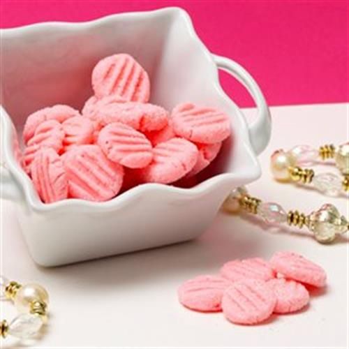 pink cookies are in a white bowl on a table next to pearls and necklaces