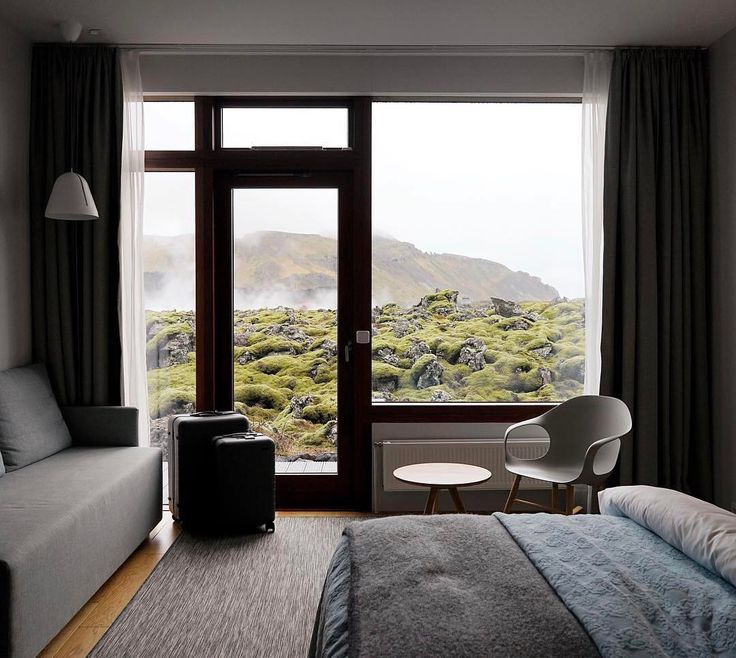 a bed room with a neatly made bed next to a large window and a chair