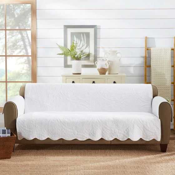 a living room with a couch covered in a white quilted cover next to a window