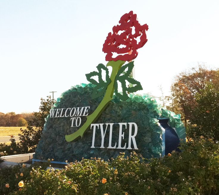 a welcome sign with a red rose on it in front of bushes and trees at the entrance to tyler