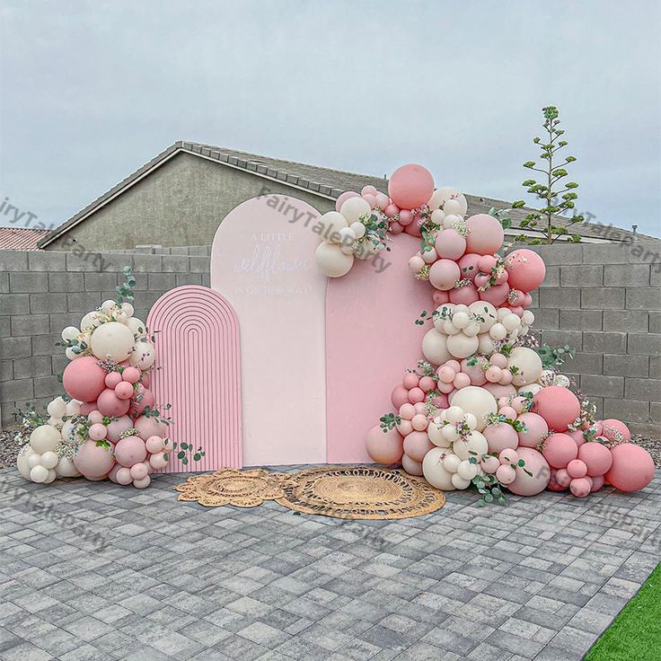 a pink and white backdrop with balloons on the ground next to a brick walkway in front of a building