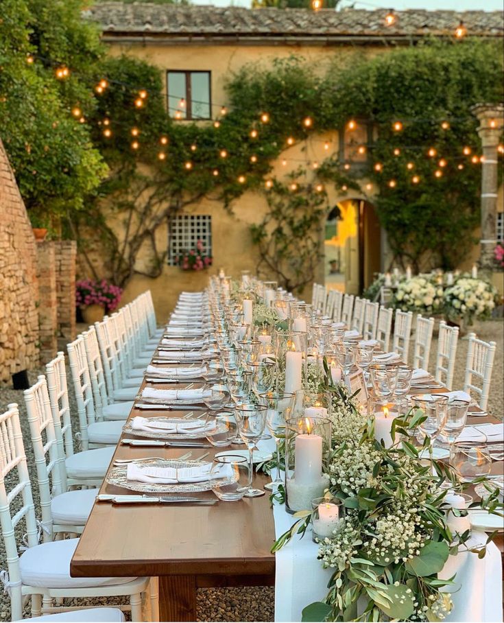 a long table is set up with white chairs and place settings for an outdoor dinner