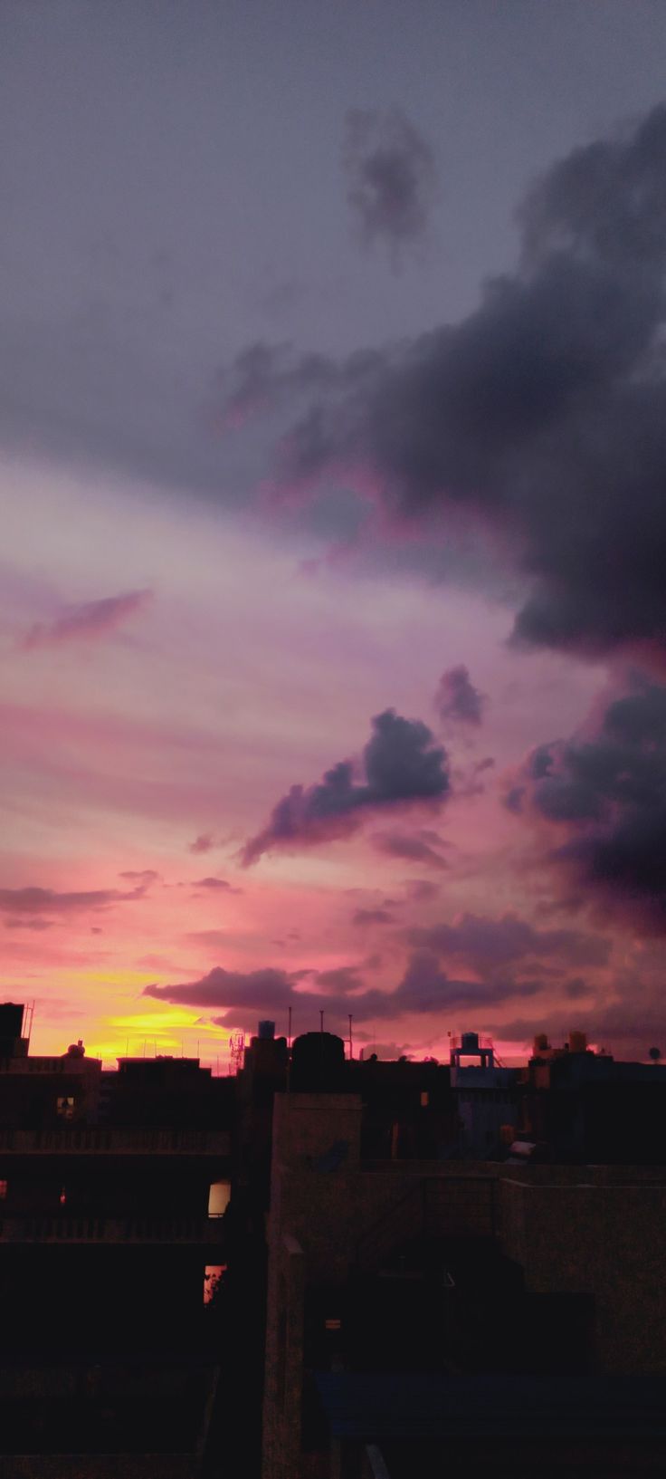 the sun is setting over some buildings and clouds