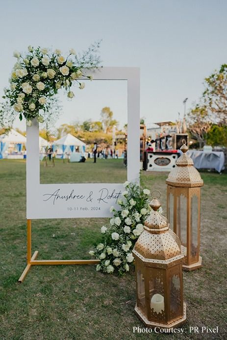 a wedding photo frame with flowers on the grass next to two lanterns and a flower arrangement