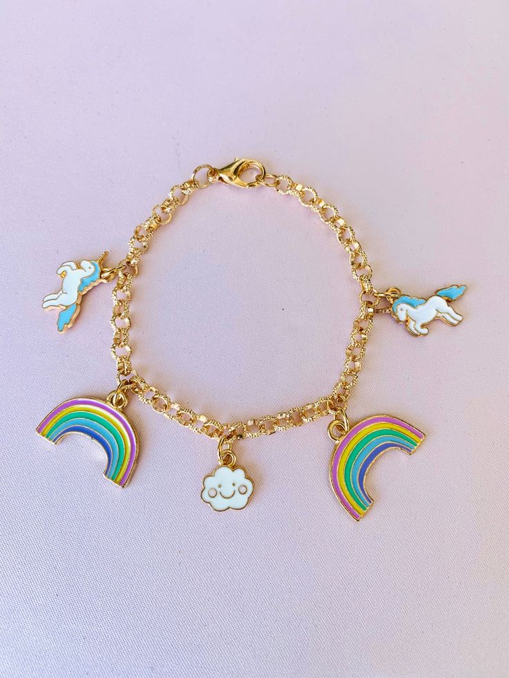 "Unicorn Rainbow Cloud Charm Bracelet This gold charm bracelet is adorable and perfect for all ages! Everyone loves unicorns! Comes with 5 charms.  *Size: 7.5\" *Charms:     (2) Blue Unicorns  (2) Pastel Rainbows  (1) Cloud *Lobster Claw Closure If you have any questions about this or any other product, don't hesitate to ask!  💕  🍭 Candy Painted Boutique 🍭" Rainbow Novelty Jewelry For Birthday, Cute Rainbow Charm Bracelet As Gift, Cute Rainbow Charm Bracelet For Gift, Rainbow Charms Bracelet As A Gift, Playful Rainbow Charm Bracelet For Gift, Playful Rainbow Charm Bracelet For Gifts, Cute Gold Bracelets With Charms, Whimsical Gold Charm Bracelet, Cute Nickel-free Rainbow Jewelry