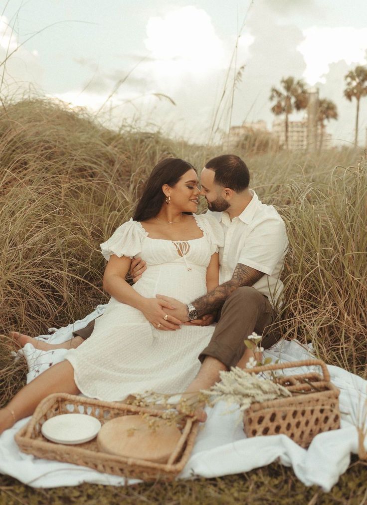 a pregnant couple sitting on a blanket in the grass