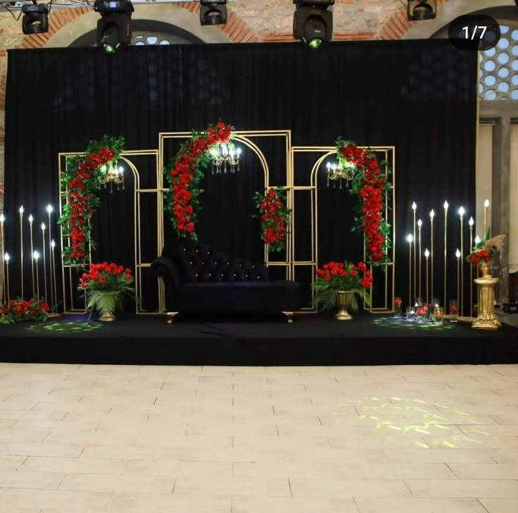 a stage set up for a wedding with red flowers and greenery on the side