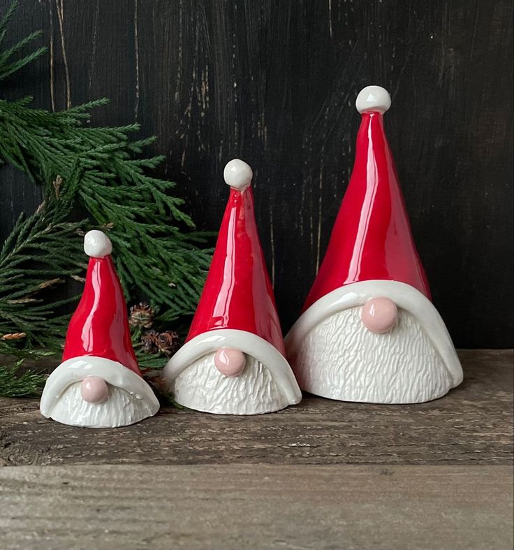 three red and white santa hats sitting on top of a wooden table next to a pine tree