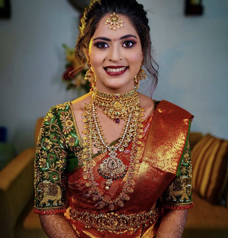 a woman in a red and green sari with gold jewelry on her neck, smiling