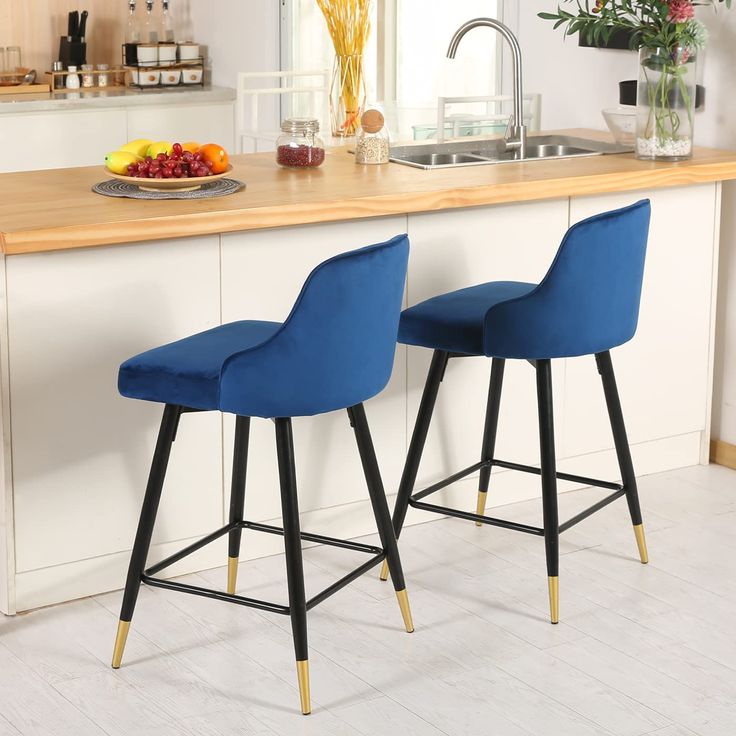 two blue bar stools sitting in front of a kitchen counter with fruit on it