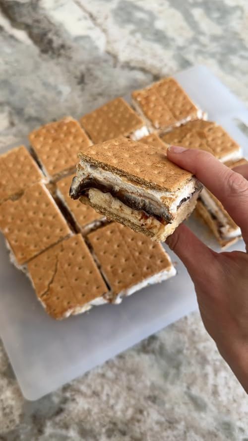 a hand holding a cracker sandwich over some crackers on a white plate and marble counter top