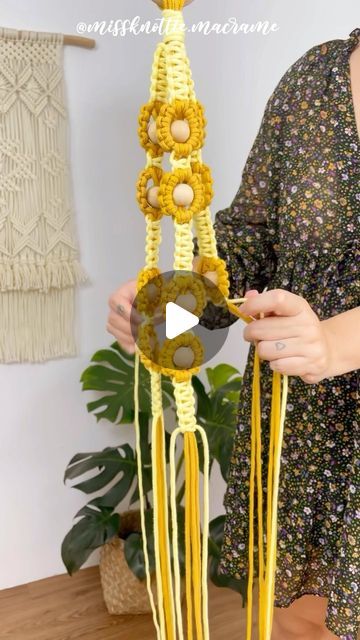 a woman is holding up a yellow crochet wind chime with beads on it