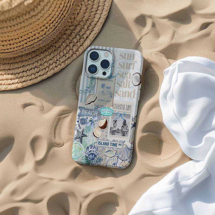 a cell phone laying on top of a sandy beach next to a straw hat and white towel