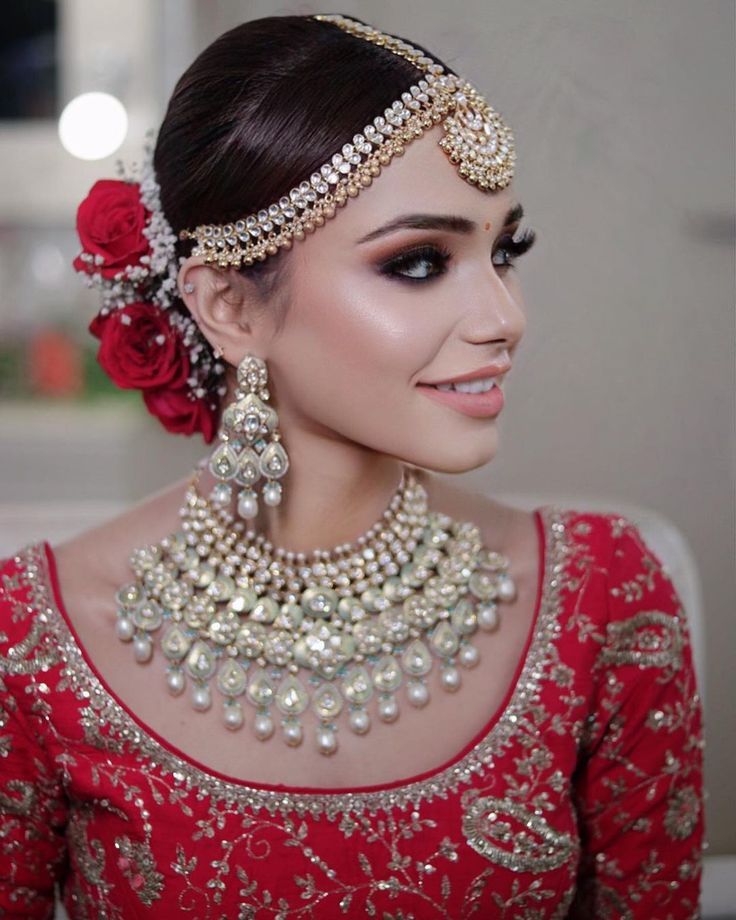 a woman wearing a red and gold outfit with pearls on her head, necklace and earrings