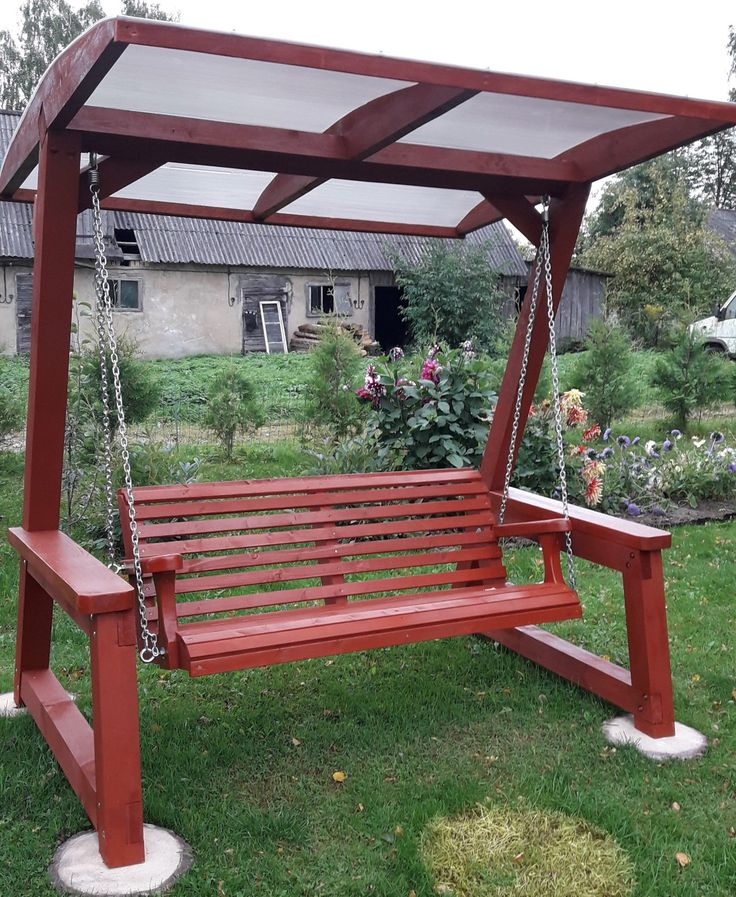 a red wooden bench sitting on top of a lush green field next to a building