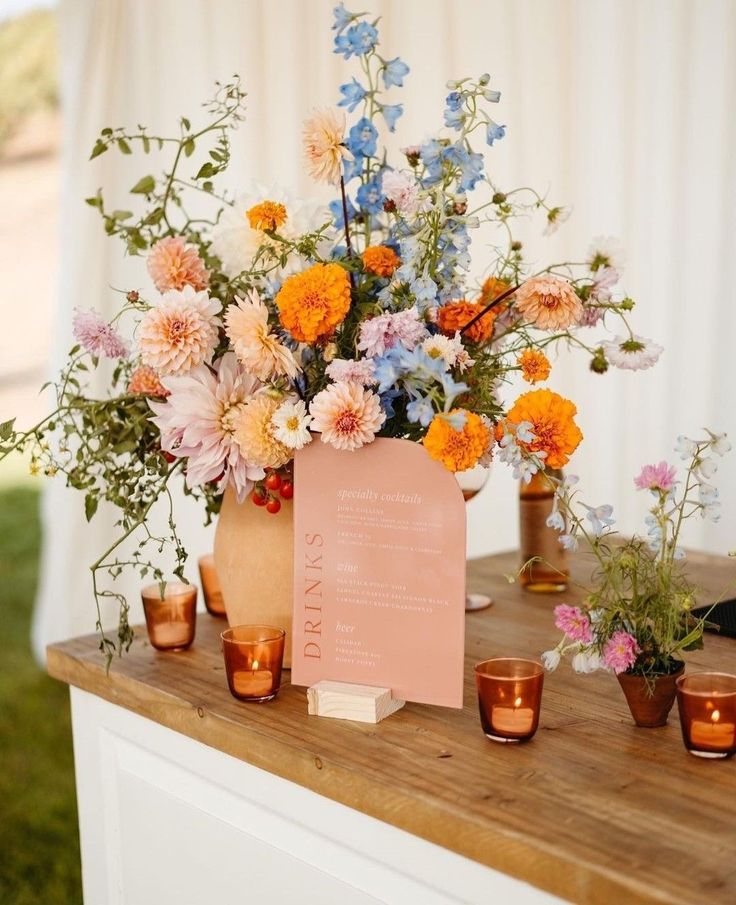 an arrangement of flowers in vases on a table with a sign and votive candles