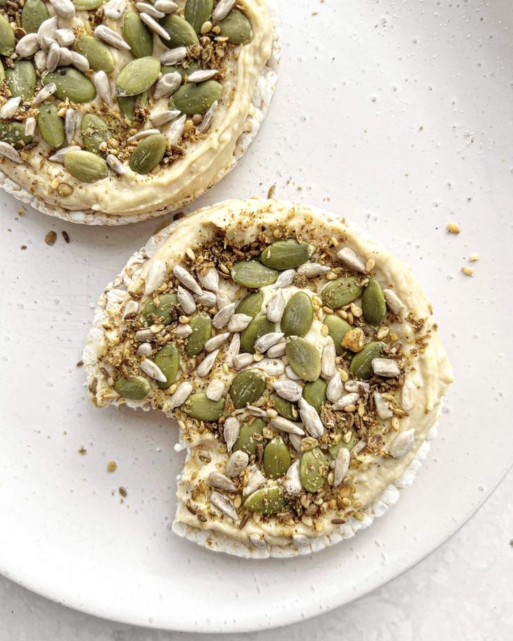 two pieces of cake with nuts and seeds on top sitting on a white plate next to each other