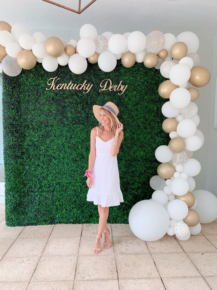 a woman standing in front of a backdrop with white and gold balloons on the wall