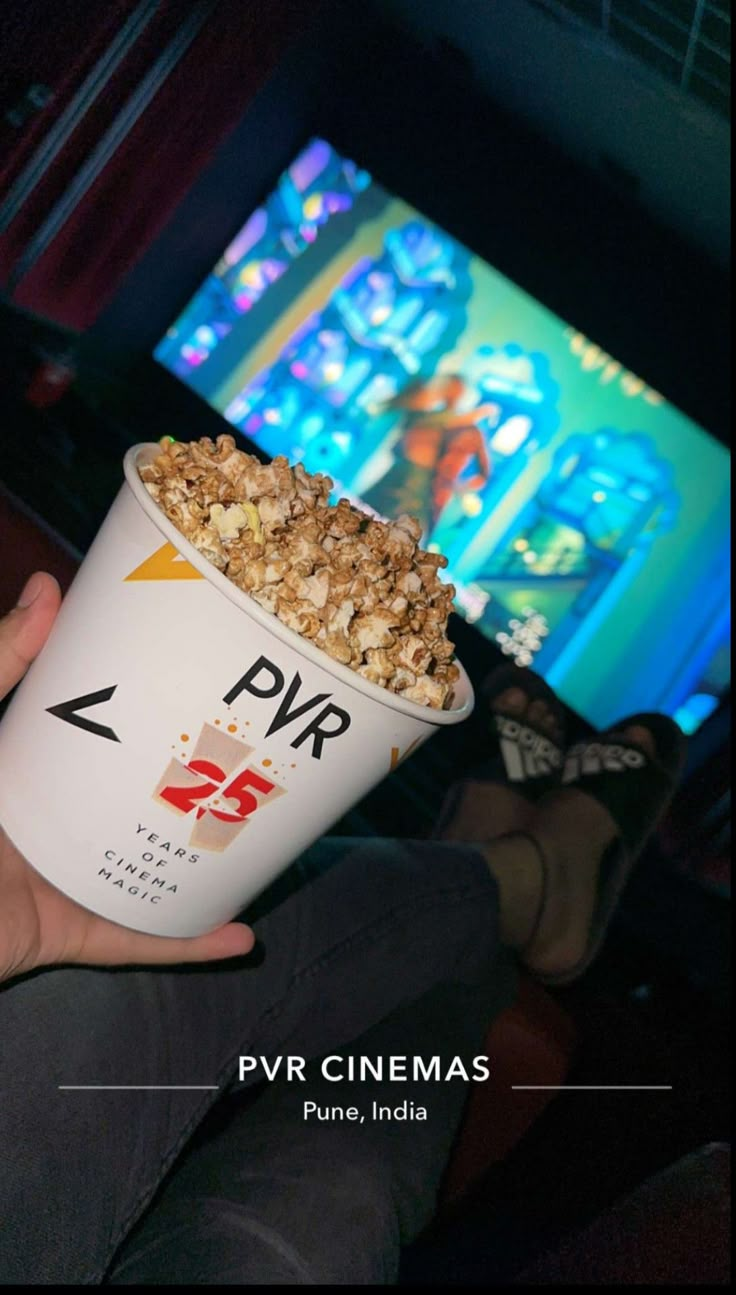 a person holding up a bowl of popcorn in front of a tv screen with the words pvr cinemas on it