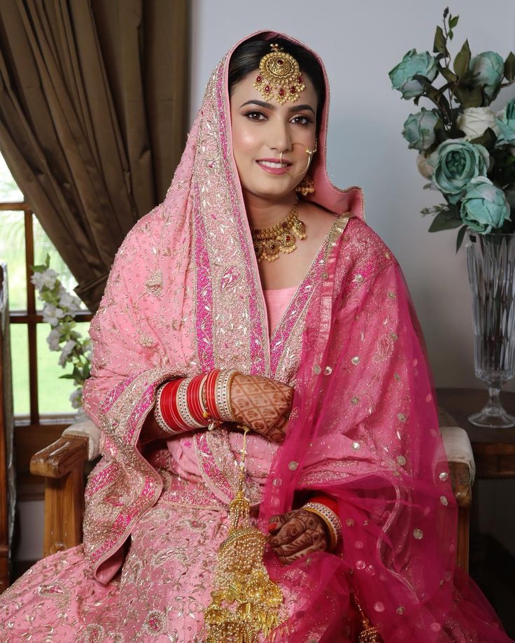 a woman in a pink bridal outfit sitting on a chair with her hands clasped