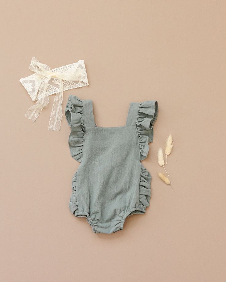 IntroducingÂ our elegant and stylish "Evelyn Romper" in sage green. The romper is made from high-quality, textured linen - like material that adds to its durability and comfort. The soft, breathable material makes it perfect for everyday wear and any special occasion. The romper features charming ruffle details that add a touch of sophistication to its overall design. The criss-cross straps on the back of the romper make it adjustable and provide a secure fit. The two-strap size options make it Green Sleeveless Bubble Romper For Spring, Gray Cotton Summer Jumpsuits And Rompers, Gray Cotton Jumpsuits And Rompers For Summer, Green Cotton Bubble Romper For The Beach, Spring Cotton Gray Jumpsuits And Rompers, Summer Cotton Bubble Romper, Summer Cotton Bubble Romper In Solid Color, Solid Color Cotton Bubble Romper For Summer, Summer Cotton Green Jumpsuits And Rompers