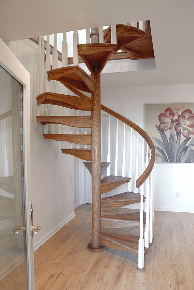 a wooden spiral staircase in an empty room with white walls and wood flooring, along with a painting on the wall