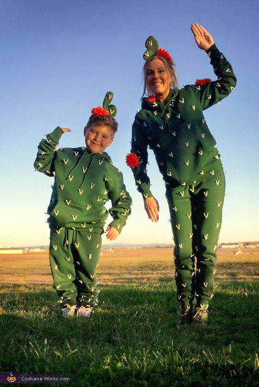 two children dressed in green cactus costumes posing for the camera with their hands up and smiling