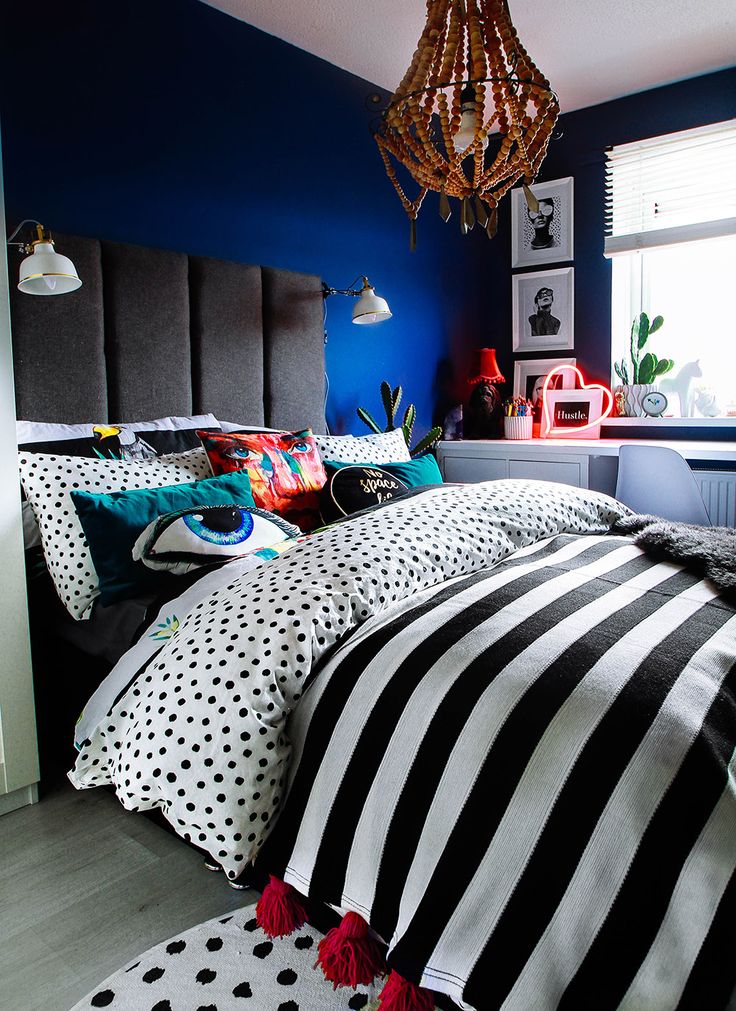 a bedroom with blue walls and black and white bedding, polka dot pillows, and a chandelier hanging from the ceiling