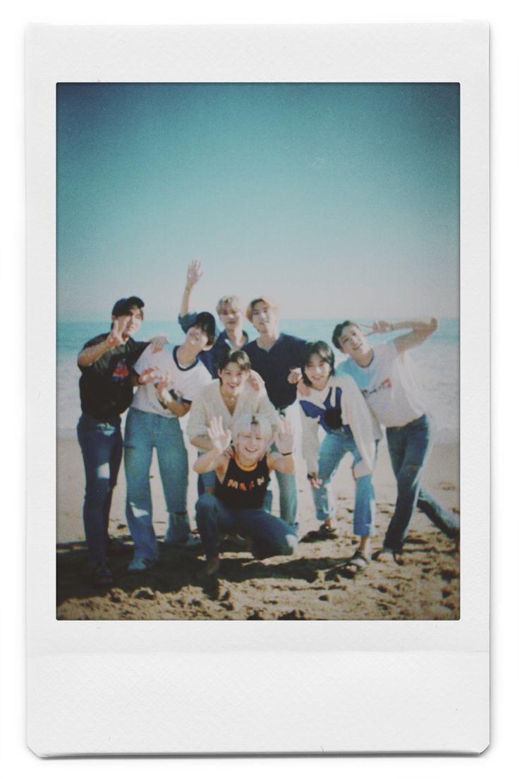 a group of people standing next to each other on top of a sandy beach near the ocean