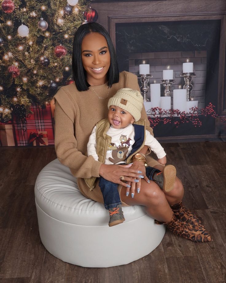 a woman holding a baby sitting on top of a white bean bag chair in front of a christmas tree