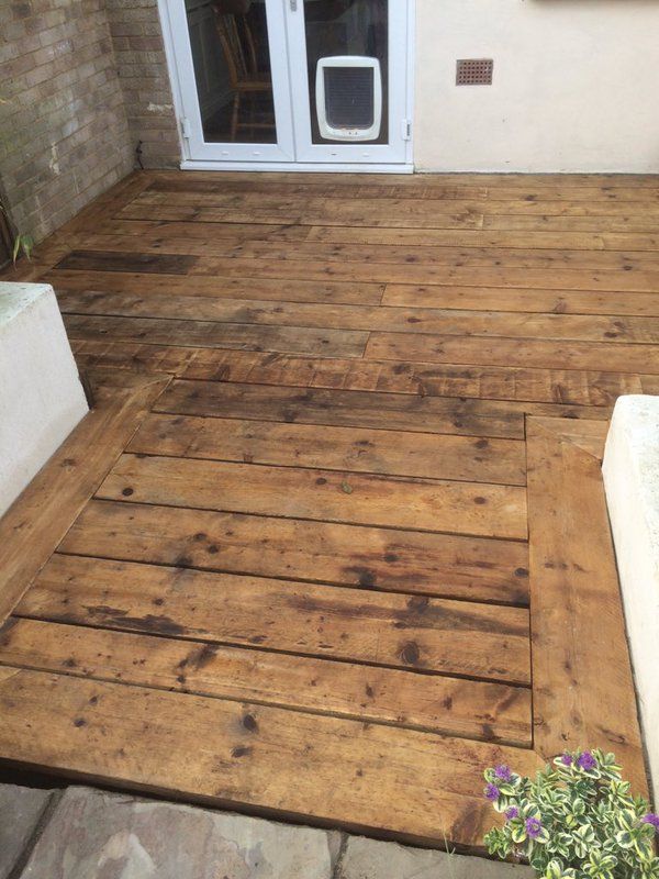 a wooden deck with a dog door on the side and flowers in the foreground