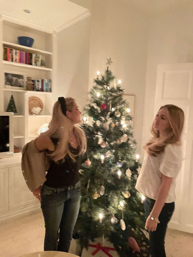 two women standing in front of a christmas tree