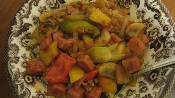 a bowl filled with meat and vegetables on top of a wooden table next to a spoon