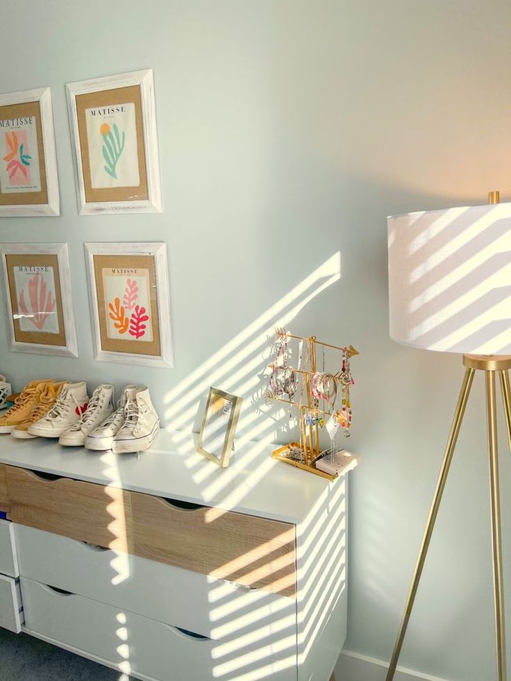 a white dresser topped with lots of shoes next to a lamp and pictures on the wall