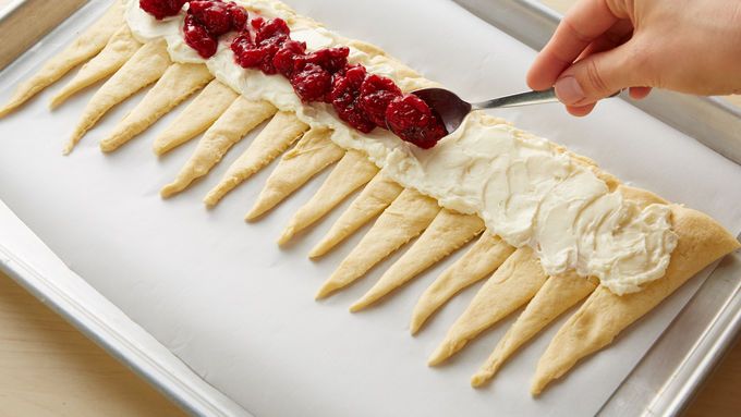 a person is spreading cream on top of some long toothpicks with raspberries