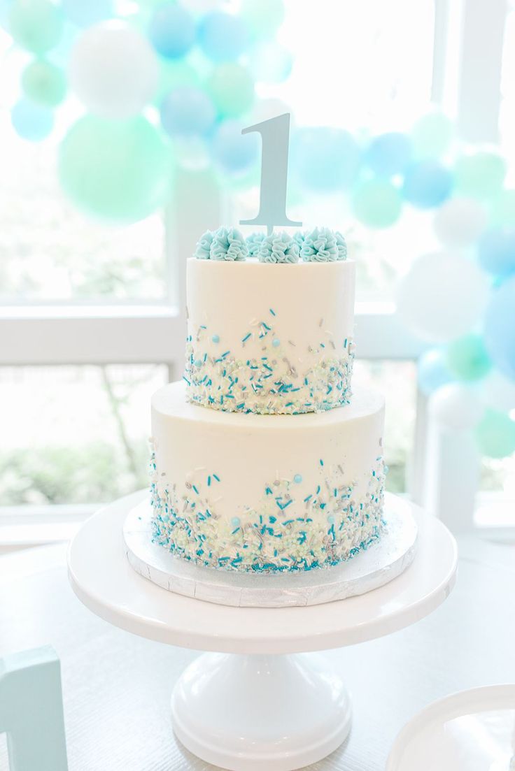 a white cake with blue sprinkles and a number one on top sitting on a table